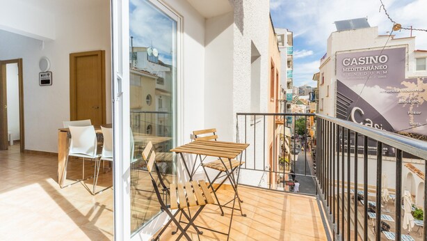 Varanda com mesa e cadeiras, porta de vidro e vista para um edifício de casino.