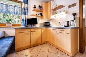A kitchen with wooden cabinets, a microwave, a kettle, and a window with a view of trees.
