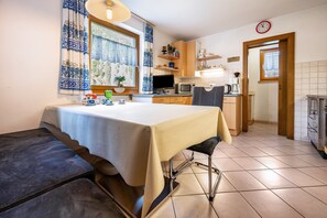 A kitchen with a dining table, chairs, a TV, and a clock on the wall.