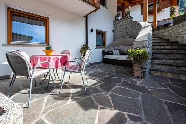 A patio with stone flooring, a table with chairs, and a bed with a stone wall backdrop.