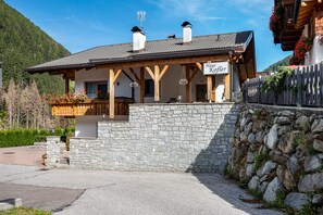 A traditional chalet with a stone wall, wooden beams, and a sign reading 'Haus Koffer.'