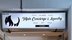 A Tapir Concierge & Laundry service entrance with a logo, a sign for free detergent and softener, a token changer, and a washing machine.