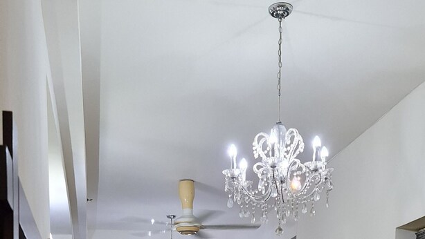 A modern living room with a black sofa, a dining table with chairs, a chandelier, and a ceiling fan.