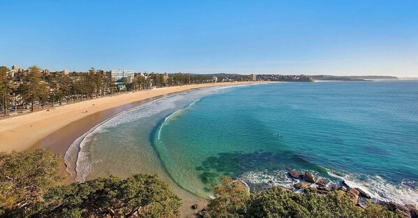 A coastal view with a beach, clear waters, and a cityscape in the background.