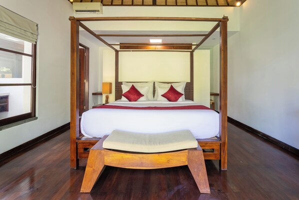 A four-poster bed with a wooden frame, white bedding, and red pillows.