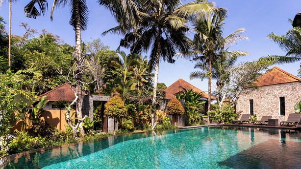 A clear swimming pool surrounded by lush greenery and traditional-style buildings. - Sukanami Villa Ubud by ecommerceloka (Payangan)