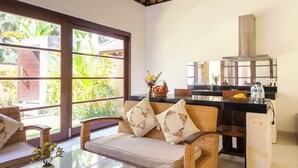 A cozy room with a wicker sofa, a glass table, and a kitchen area with a counter and a stove. - Sukanami Villa Ubud by ecommerceloka (Payangan)