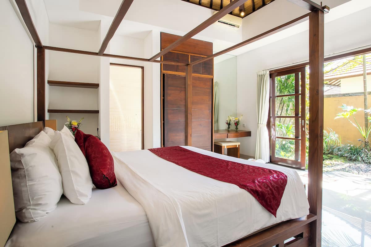 A bedroom with a wooden four-poster bed, white bedding, and a red throw blanket.
