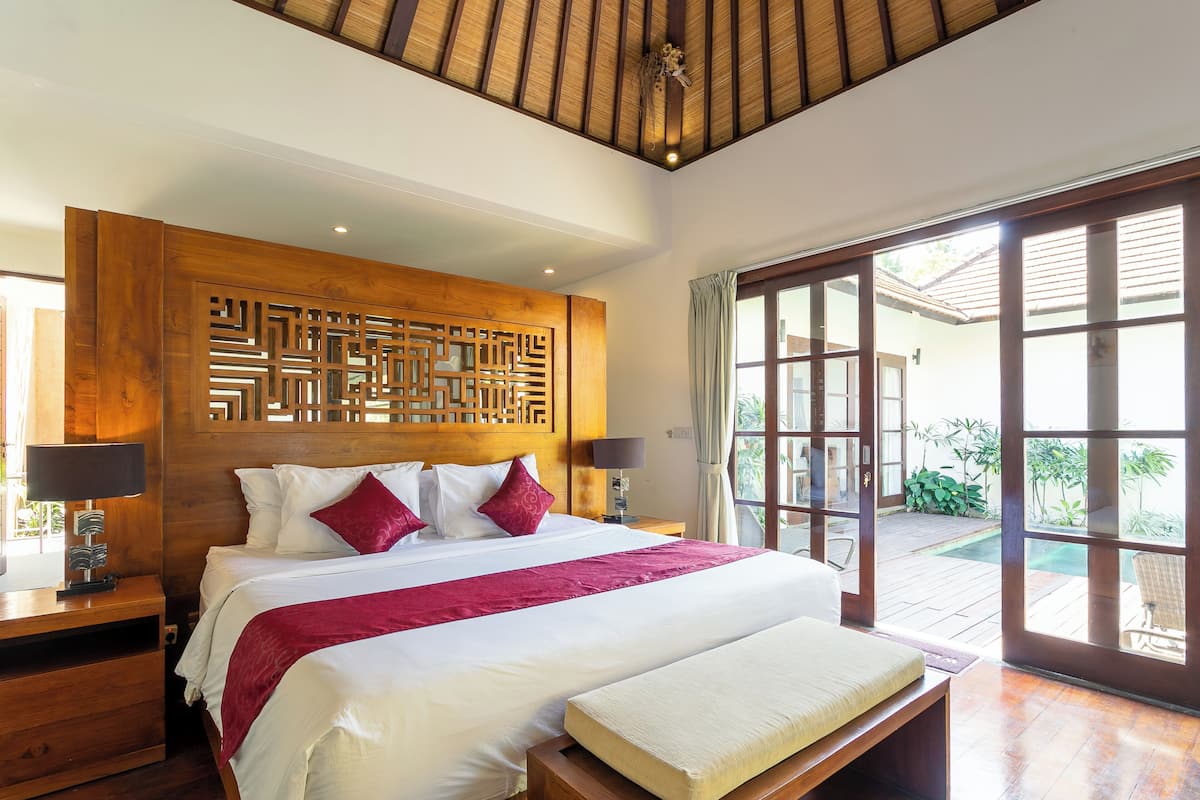 A spacious bedroom with a large bed, wooden headboard, and a view of the outdoor area through a sliding door.