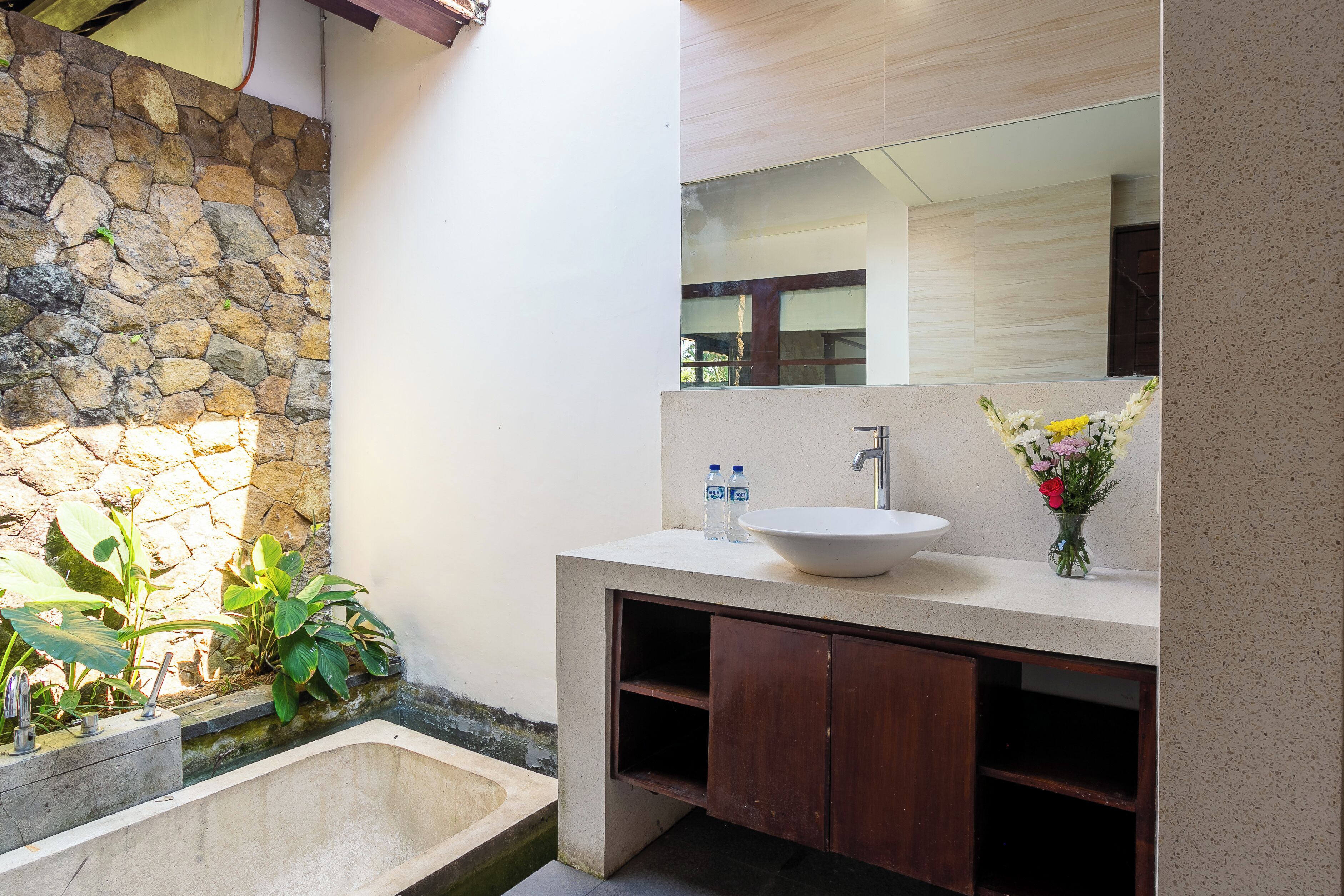 A bathroom with a stone wall, a white sink, wooden cabinets, and a mirror.