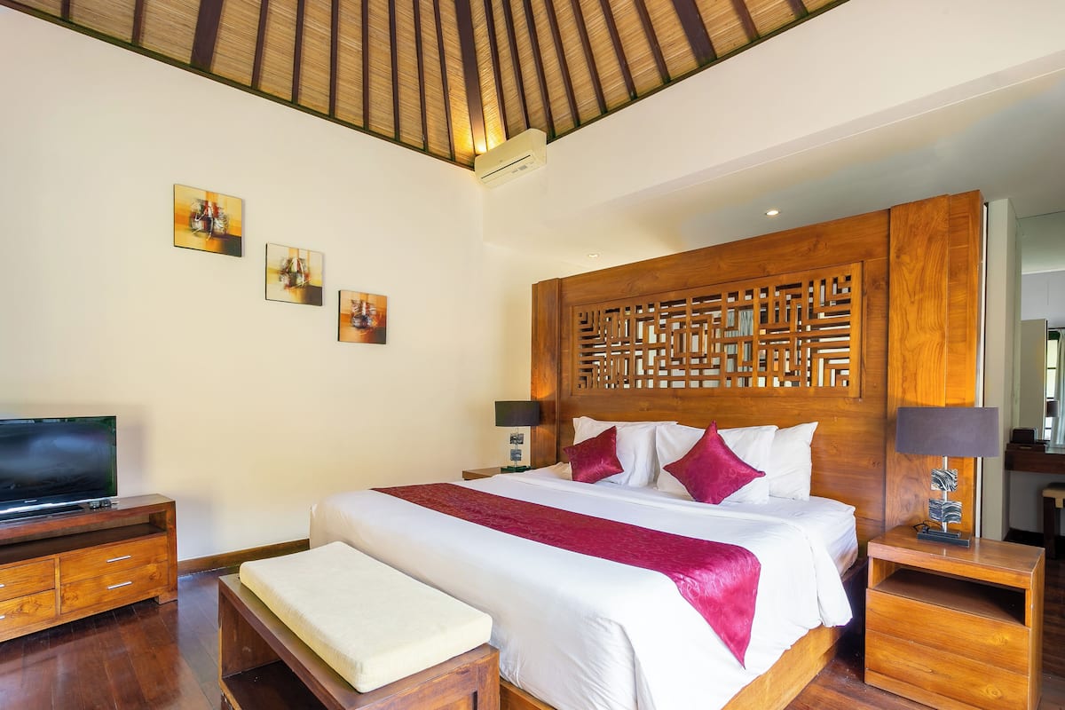 A hotel room with a large bed, wooden headboard, a flat-screen TV, and artwork on the wall.