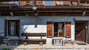 Un edificio rustico con balconi in legno, una panchina e un tavolo all'esterno.