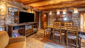 Un interno rustico con parete in pietra, soffitto in legno, un tavolo da pranzo con sedie, una televisione e una libreria.