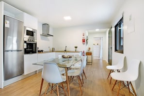 Une cuisine moderne dotée d’appareils électroménagers en acier inoxydable, d’une table à manger en verre et de chaises blanches.