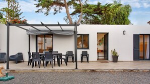 Een modern terras buiten met een tafel, stoelen, een pergola en een bloempot.
