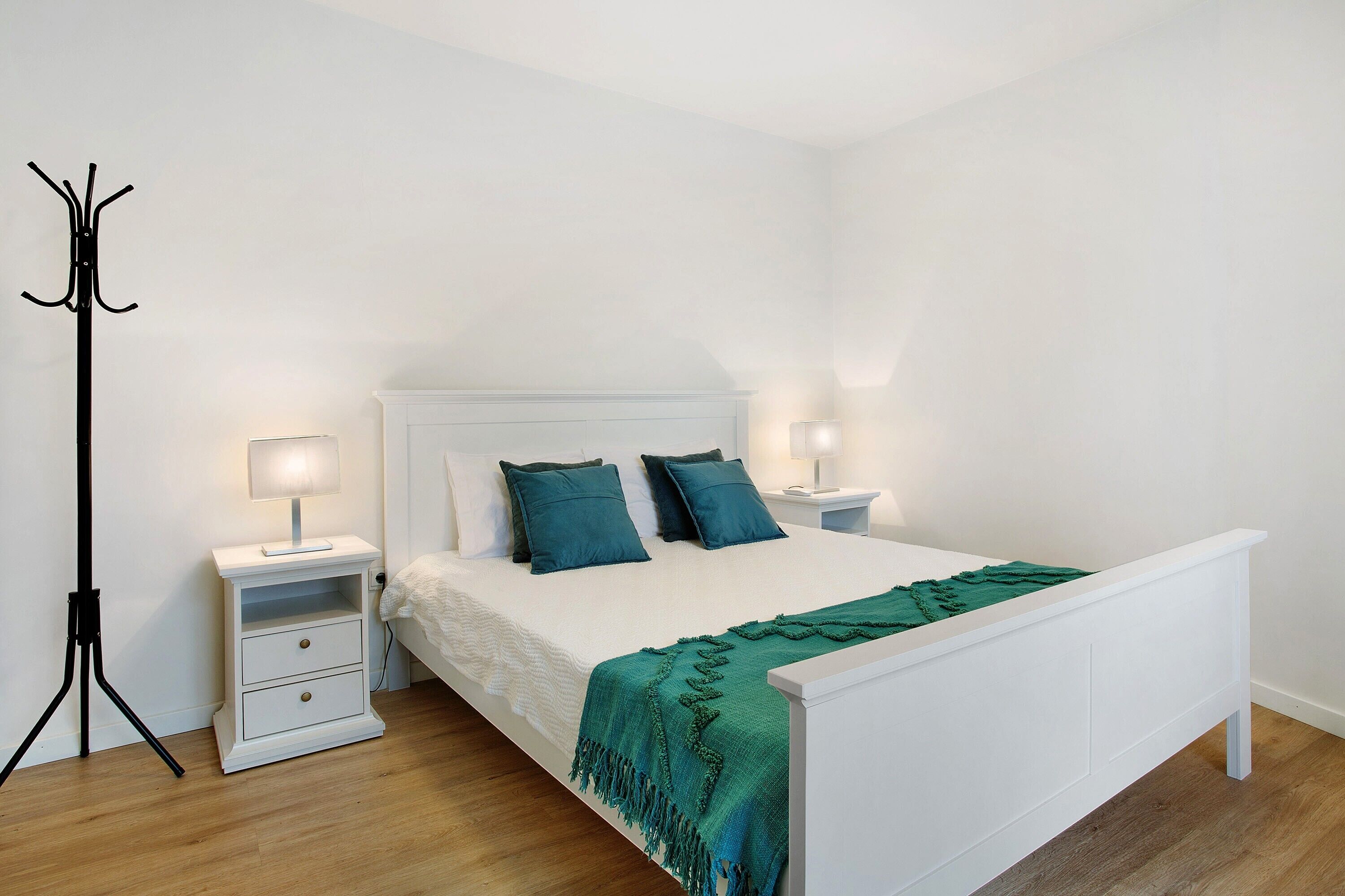 A neatly arranged bedroom with a white bed, two bedside tables, a floor lamp, and a green throw blanket.