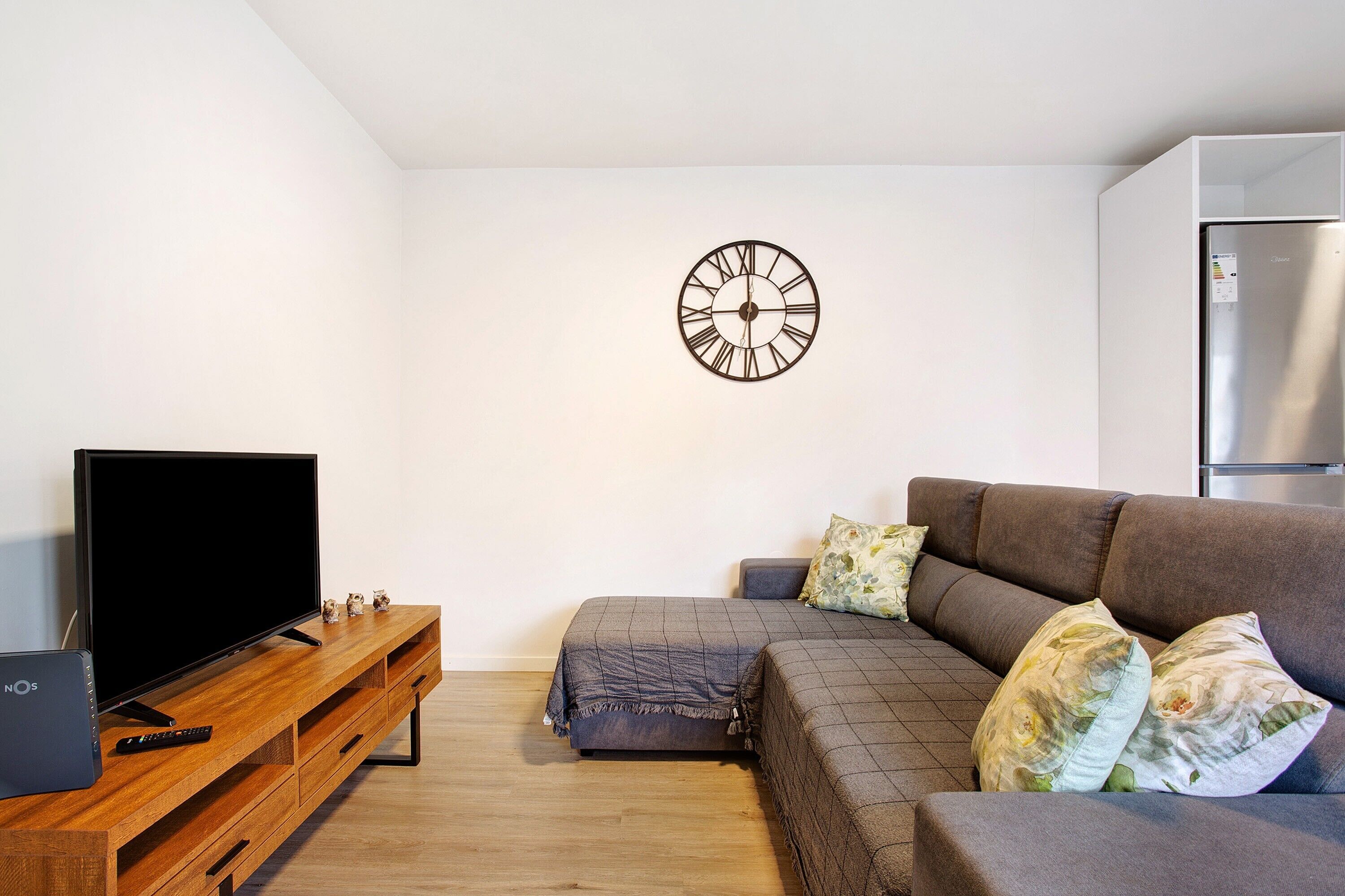 A modern living room with a flat-screen TV, wooden entertainment unit, sofa, and a wall clock.