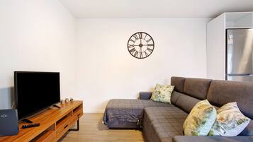 A modern living room with a flat-screen TV, wooden entertainment unit, sofa, and a wall clock.