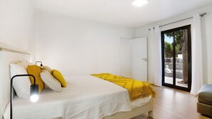 Een slaapkamer met een bed, een bedlampje, een bank en een schuifdeur naar een buitenruimte.