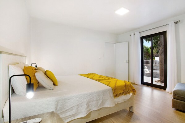 Une chambre à coucher comprenant un lit, une lampe de chevet, un canapé et une porte-fenêtre coulissante donnant sur un espace extérieur.