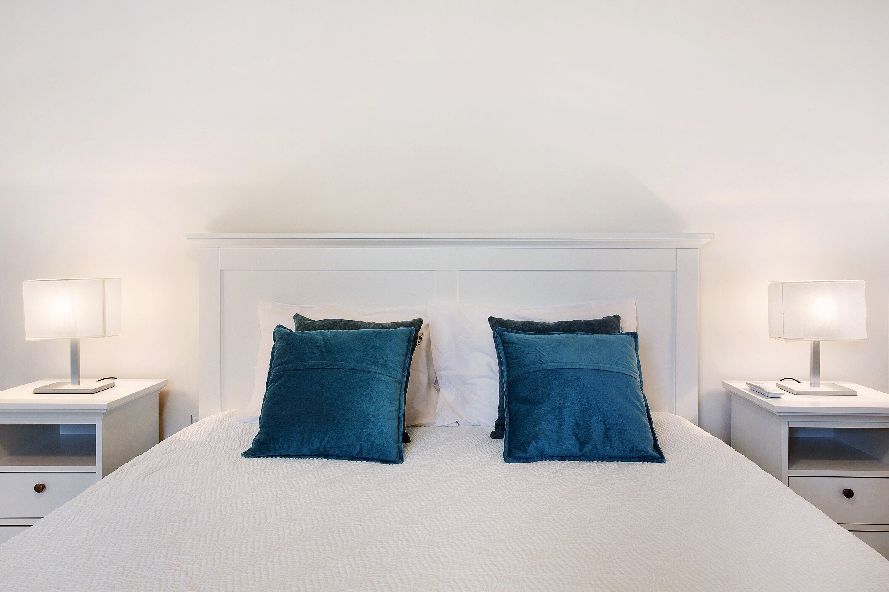 A neatly made bed with two pillows, two bedside tables with lamps, and a white headboard.