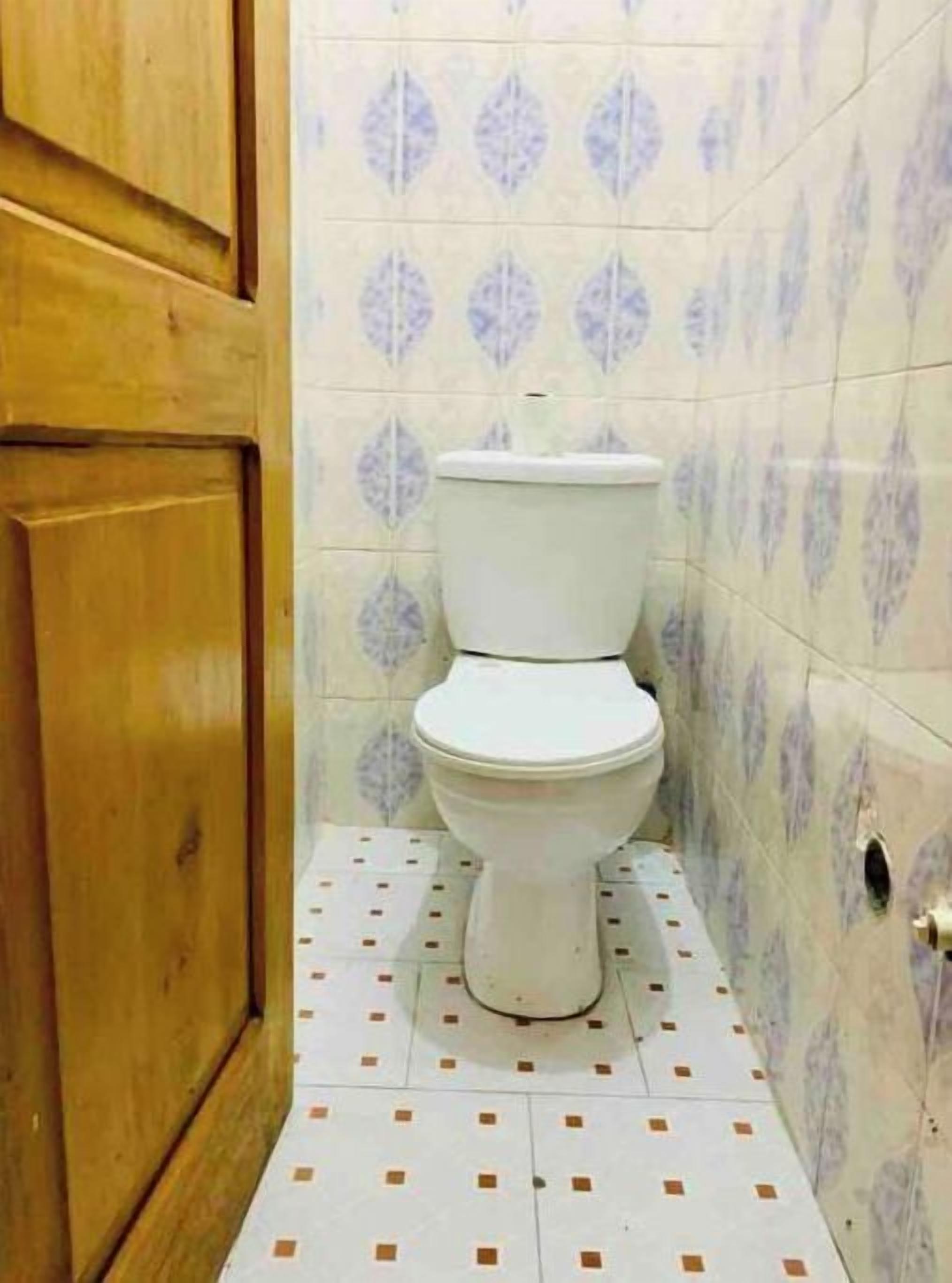 Un baño con inodoro, puerta de madera y baldosas estampadas en paredes y suelo.