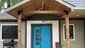 Un porche abrité avec une porte bleue, un barbecue et une chaise.