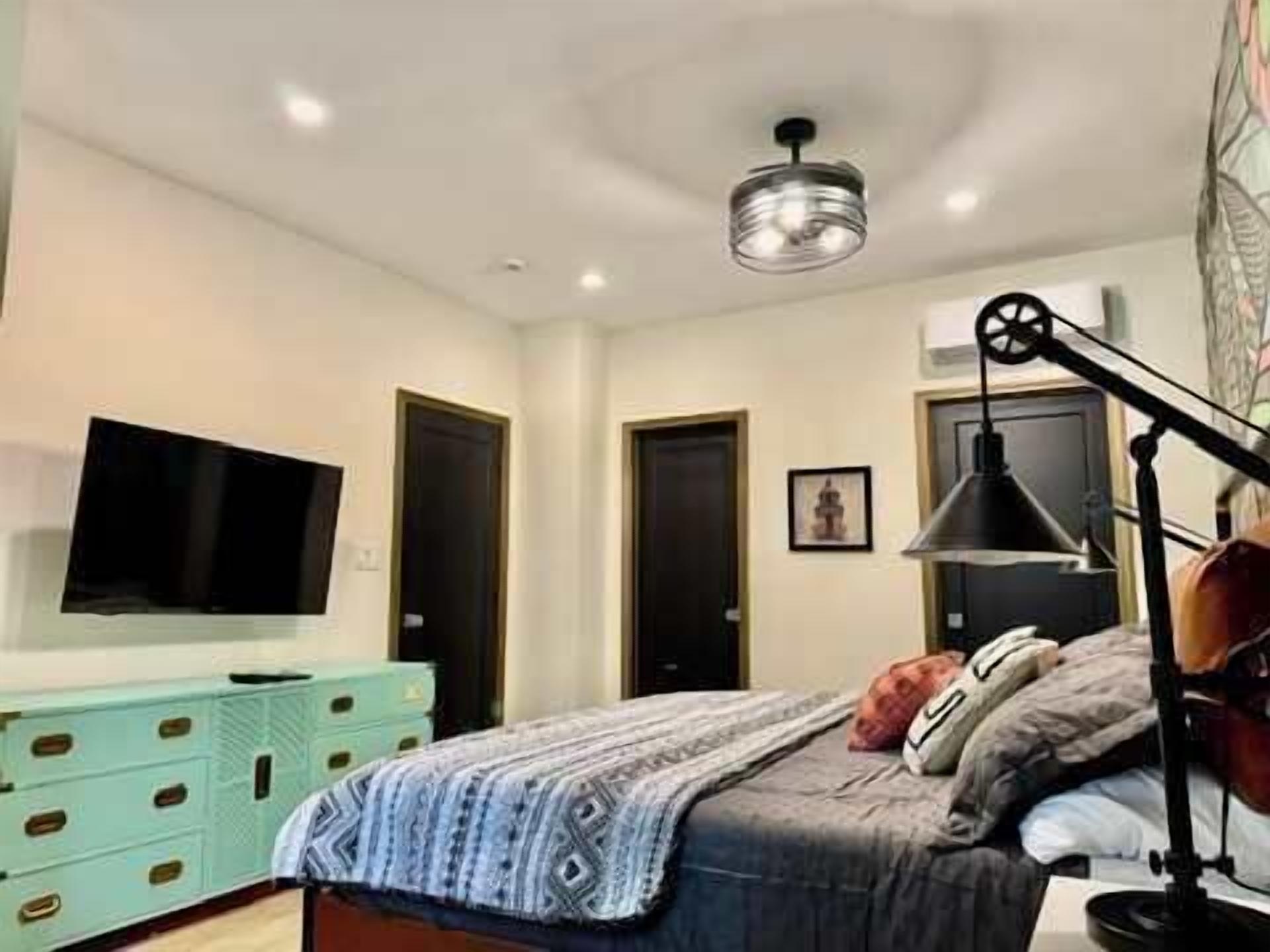 A bedroom with a bed, a television, a desk lamp, and a dresser.