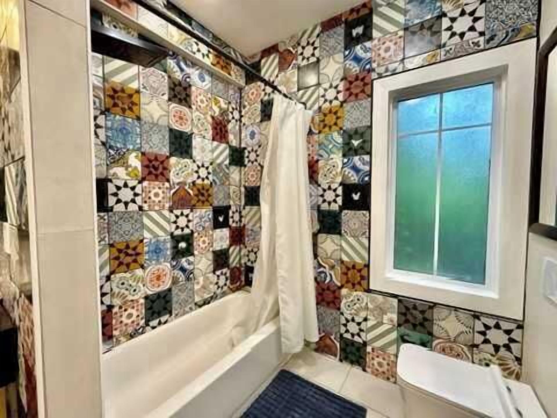 A bathroom with a patterned tile wall, a bathtub, a window, and a shower curtain.