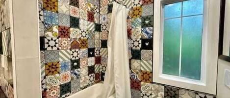 A bathroom with a patterned tile wall, a bathtub, a window, and a shower curtain.