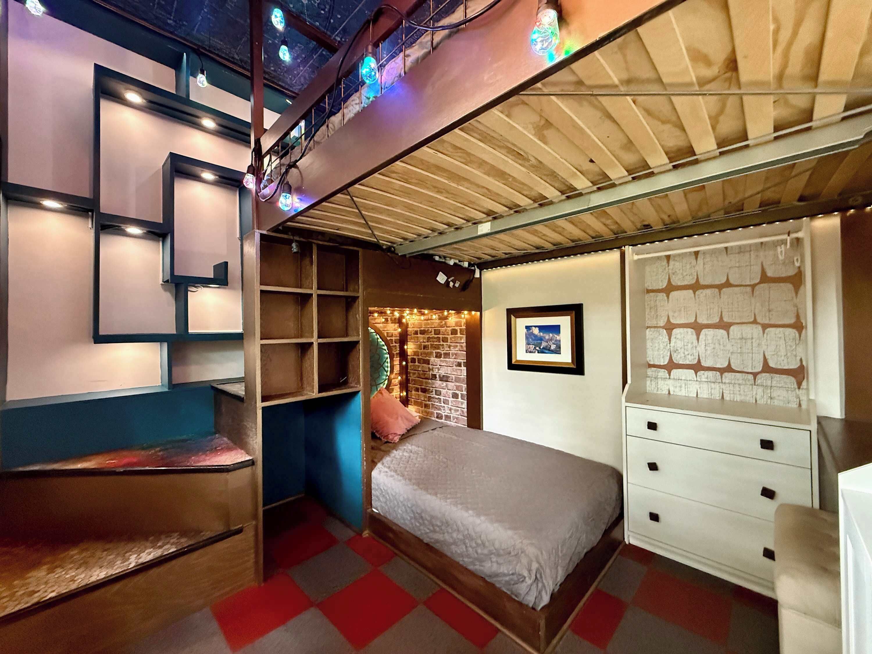 Ein Zimmer mit einem Bett, einem Schminktisch, einem Regal und einer Ziegelwand.