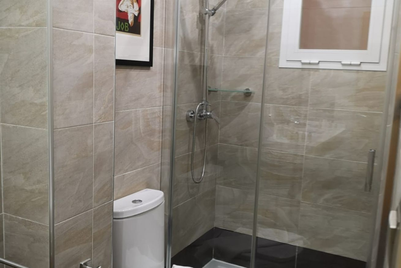 Ein kleiner, abgeschlossener Duschbereich mit Glastür, einer weißen Toilette und einem gerahmten Bild an der Wand.