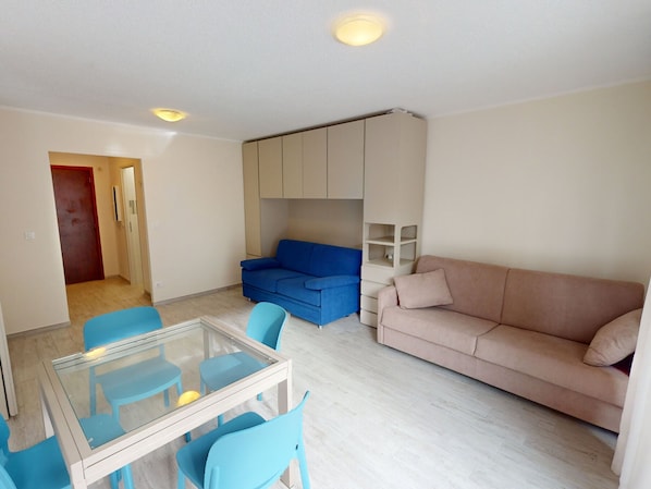 Cozy living space with a glass-top dining table, beige sofa, and blue couch.