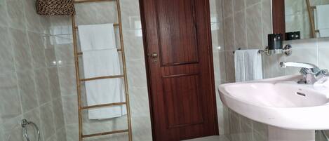 Un baño con puerta de madera, lavamanos blanco, espejo y perchero.