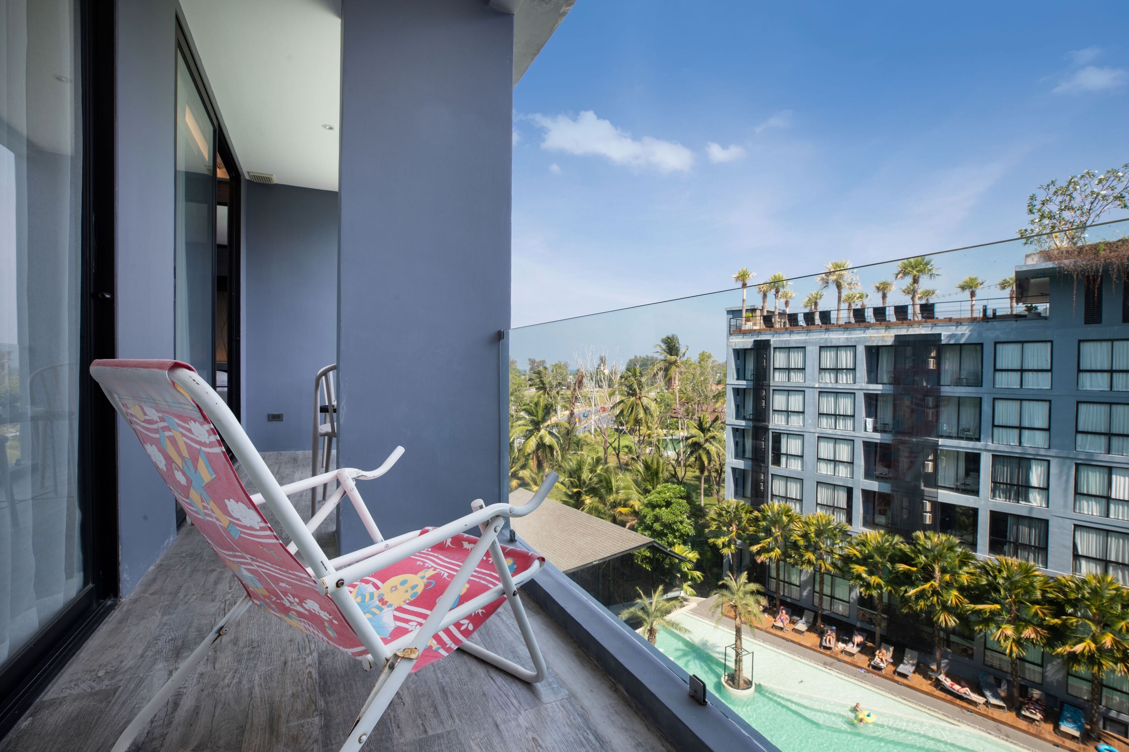 Un balcon avec une chaise blanche, une vue sur une piscine et un immeuble à plusieurs étages doté de balcons.