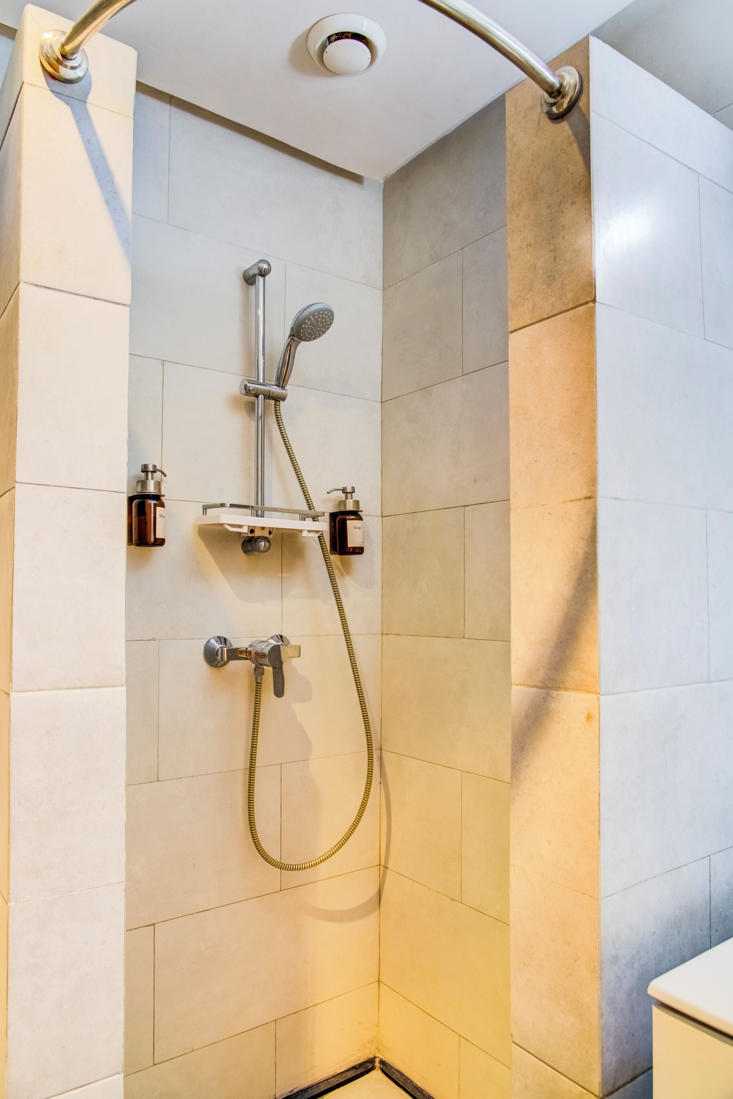 Une douche équipée d’un pommeau de douche et d’un flexible à main, le tout fixé sur un mur carrelé avec un angle décoratif.