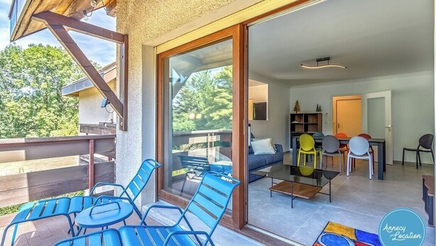 A modern interior with a balcony, a dining area, and a living room with a sofa and chairs.