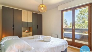 A bedroom with a large bed, wooden cabinets, a small table, and a sliding glass door to the outside.