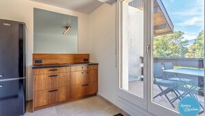 A modern kitchen with a black refrigerator, wooden cabinets, and a large window overlooking a balcony with outdoor furniture.