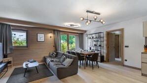 Un salon moderne avec un canapé, une table à manger et des chaises. On y trouve également un téléviseur, une bibliothèque et une fenêtre avec des rideaux.