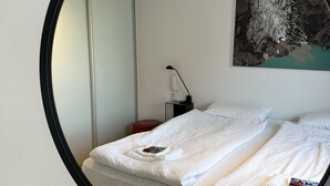 Un lit bien fait, avec du linge de lit blanc, une petite table de chevet avec une lampe et un tableau accroché au mur.