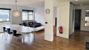 Un salon moderne comprenant un coin repas, un canapé agrémenté de coussins à motifs, une table de salle à manger ronde avec des chaises, un luminaire suspendu et un extincteur fixé au mur.