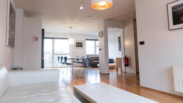 Un salon moderne avec un canapé blanc, une table à manger avec des chaises, un lustre et un extincteur fixé au mur.