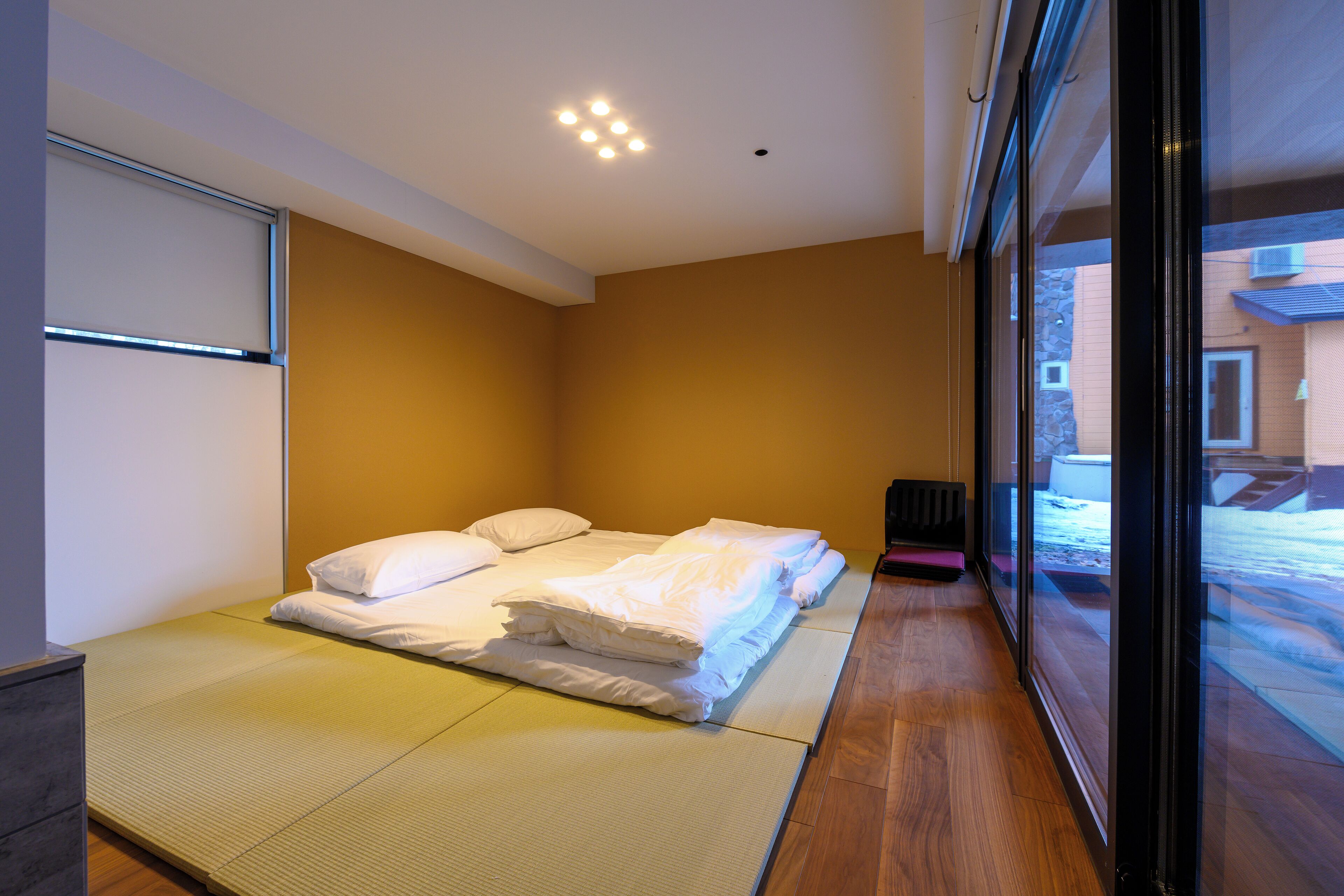 A room with tatami mats, a bed with white bedding, and a view through a glass door.