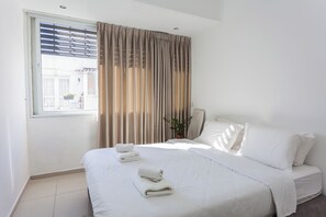 Ein Hotelzimmer mit Bett, weißen Leinen, einem Fenster mit Vorhängen und einer Zimmerpflanze.