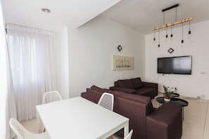 Ein modernes Wohnzimmer mit einem weißen Tisch, braunen Sofas, einem an der Wand montierten Fernseher und einer Deckenleuchte.