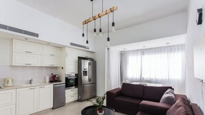 Een moderne keuken met witte kastjes, een roestvrijstalen koelkast en een koffieapparaat. Er staat een bruine bank en een klein tafeltje met een plantje.