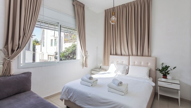 Een slaapkamer met een bed, een nachtkastje, een lamp en een raam met gordijnen.