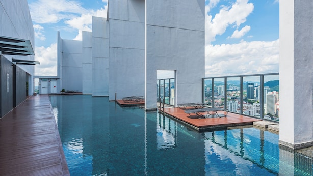 Una piscina infinita con terraza de madera, arquitectura moderna y vista a la ciudad.