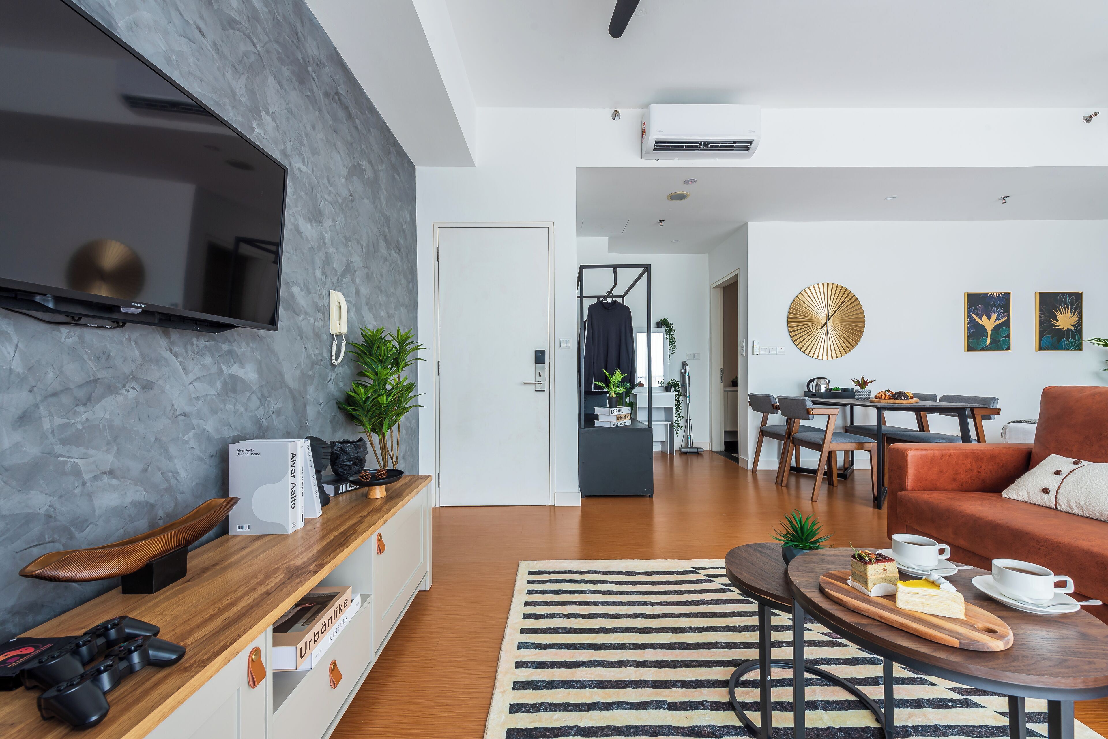 Een moderne woonkamer met een flatscreen televisie, een gameconsole en een eethoek met een tafel en stoelen.